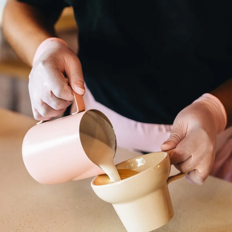 Barista pouring milk into takeaway cups