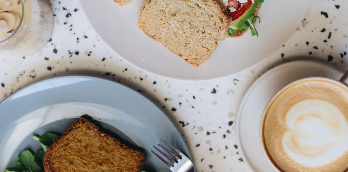 Overhead brunch spread at The Family Bakehouse — fresh bread, a salad plate and a cappuccino with latte art